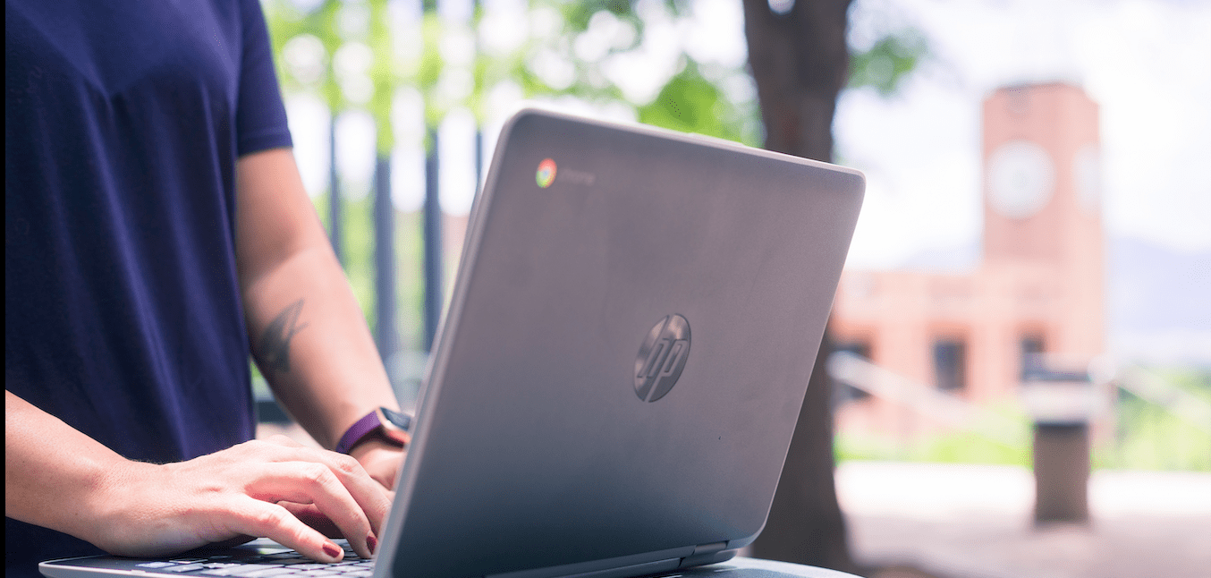 A person using a laptop in front of the UCCS clock tower. 